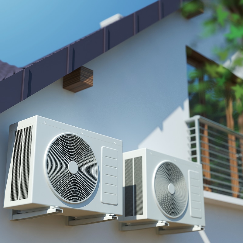 Deux unités de climatisation blanches modernes sont installées sur la façade d'une maison sous un ciel bleu clair.
