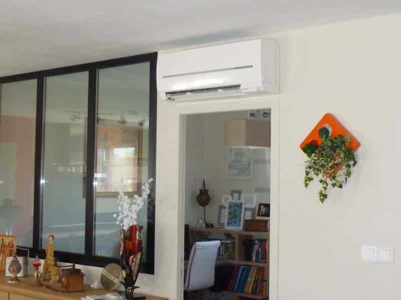 Intérieur moderne: climatiseur mural blanc, verrière sombre, meuble décoré. Pot mural orange avec plantes et interrupteurs sur mur clair.