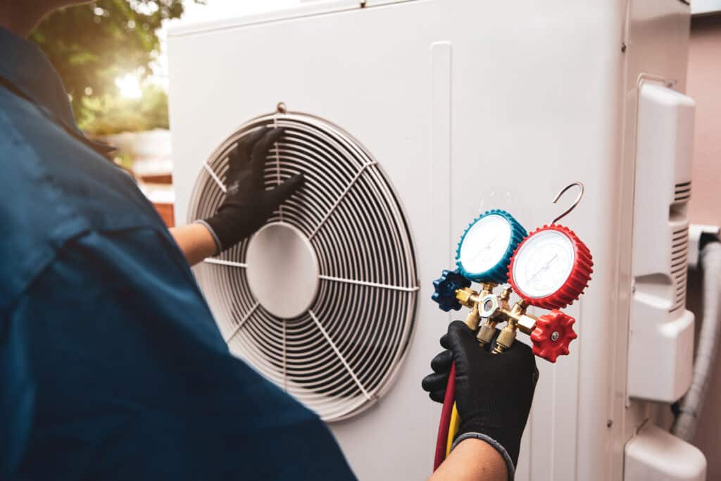 Technicien en gants vérifie le ventilateur d'une unité de climatisation extérieure et tient des manomètres pour l'entretien.