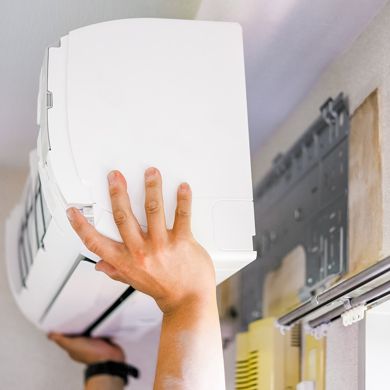 Mains d'un technicien installant ou ajustant une unité intérieure de climatisation murale blanche sur son support.