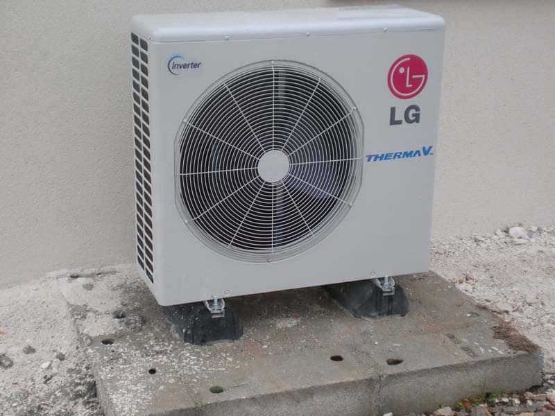 Unité extérieure de pompe à chaleur LG Therma V Inverter blanche avec ventilateur, posée sur dalle béton près d'un mur.