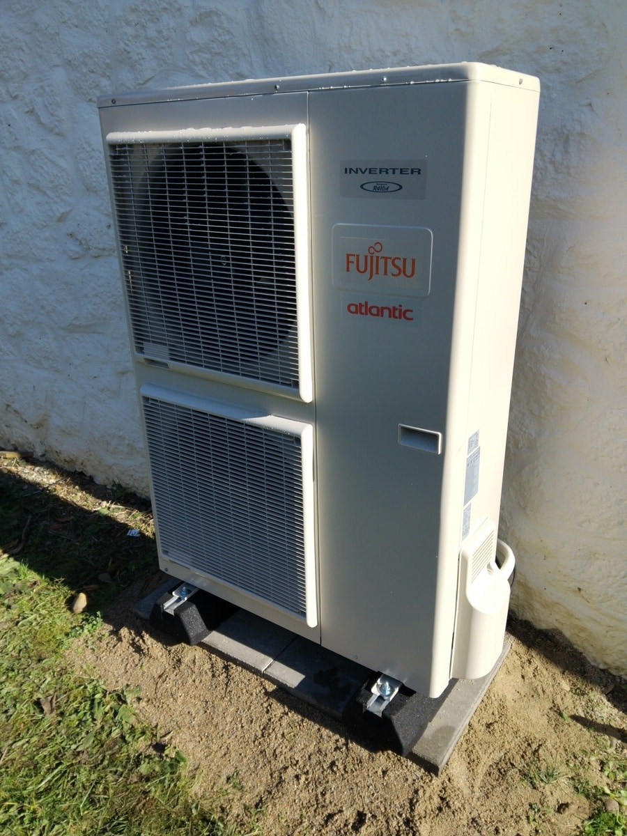 Unité extérieure de pompe à chaleur Fujitsu Atlantic Inverter R410A beige, installée sur des dalles au sol contre un mur blanc texturé.